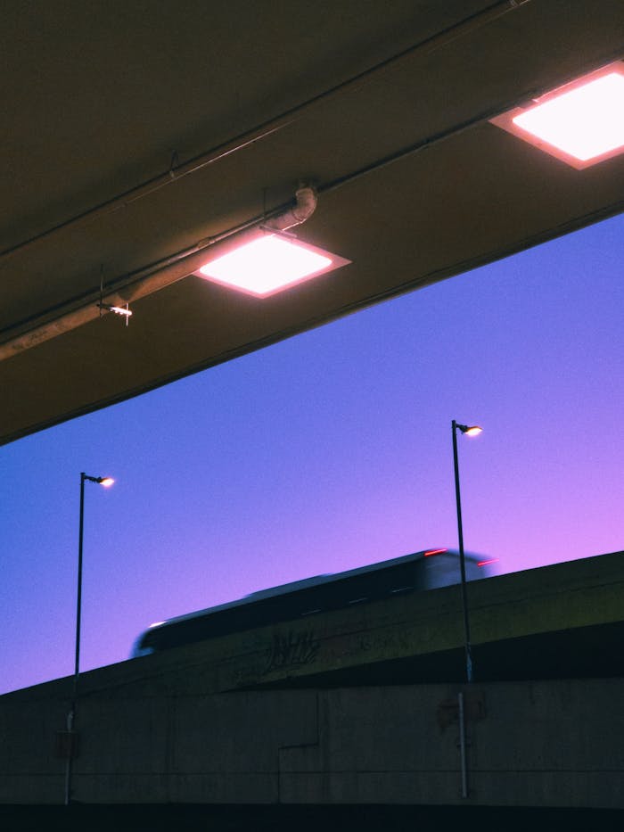 A blurred bus drives over an overpass in Belo Horizonte at twilight, under vibrant city lights.