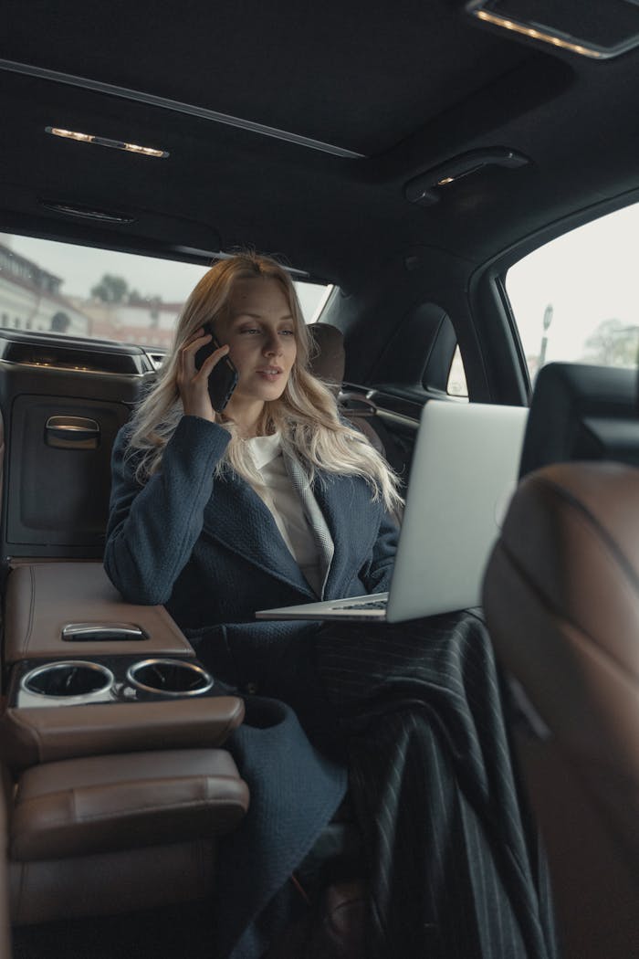 services-02 Confident businesswoman making a call and working on a laptop in a luxury car interior.